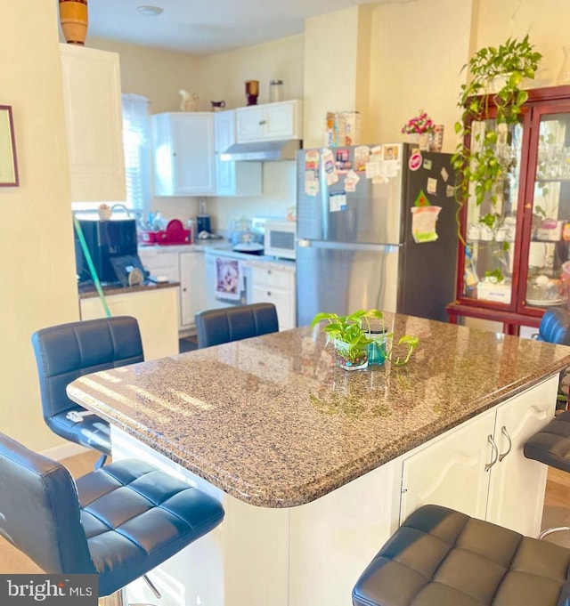 kitchen with a breakfast bar area, white cabinetry, stone counters, and stainless steel refrigerator