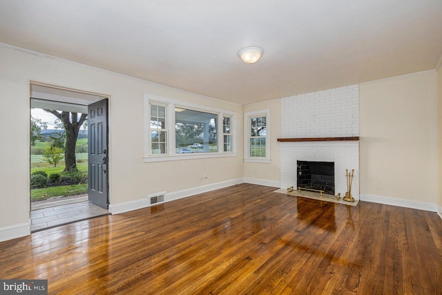 unfurnished living room with plenty of natural light, wood-type flooring, crown molding, and a brick fireplace