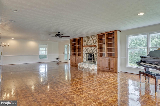 unfurnished living room with ceiling fan with notable chandelier, a stone fireplace, built in features, and a textured ceiling