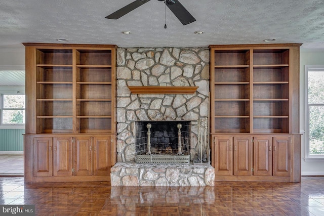 unfurnished living room with a textured ceiling, a stone fireplace, plenty of natural light, and crown molding