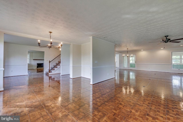 spare room featuring ceiling fan with notable chandelier, dark parquet flooring, and a textured ceiling