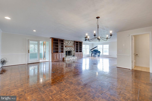 unfurnished living room with french doors, ornamental molding, a textured ceiling, an inviting chandelier, and a stone fireplace