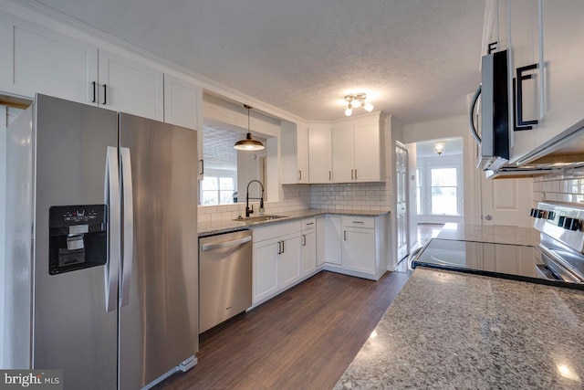 kitchen featuring light stone counters, stainless steel appliances, sink, decorative light fixtures, and white cabinetry