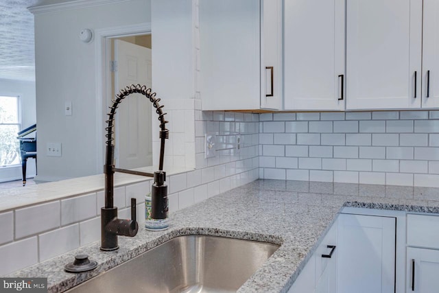 interior details with decorative backsplash, light stone counters, white cabinetry, and sink