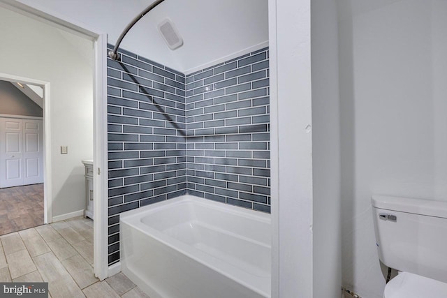 bathroom featuring tiled shower / bath combo, toilet, and vaulted ceiling