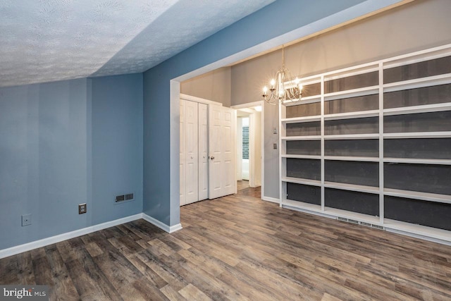 empty room featuring dark hardwood / wood-style flooring, a chandelier, and a textured ceiling