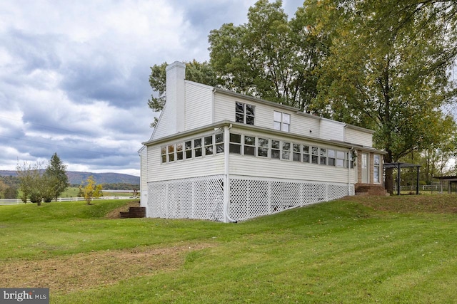 rear view of house with a lawn, a sunroom, and a mountain view