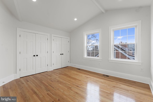 unfurnished bedroom with lofted ceiling with beams, two closets, and light hardwood / wood-style flooring