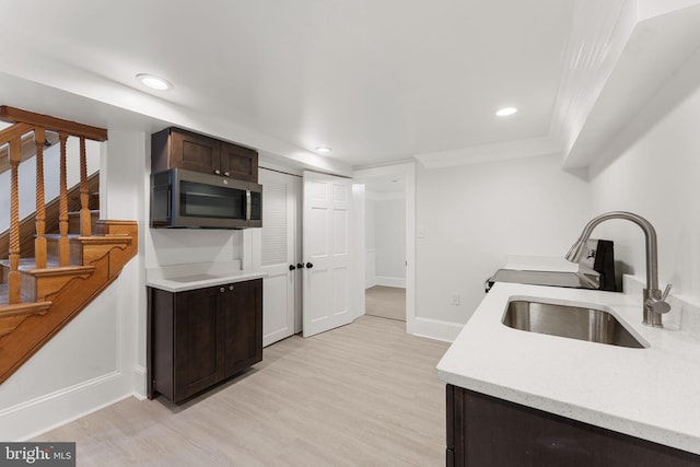 kitchen with dark brown cabinetry, sink, ornamental molding, and light hardwood / wood-style floors