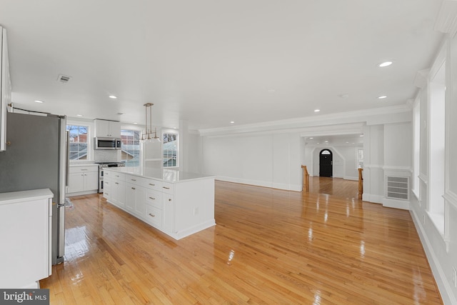 kitchen featuring crown molding, light wood-type flooring, appliances with stainless steel finishes, a kitchen island, and white cabinets