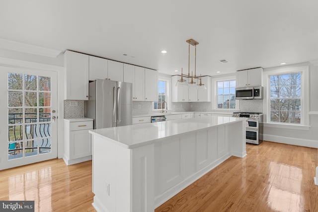 kitchen with hanging light fixtures, appliances with stainless steel finishes, a kitchen island, light hardwood / wood-style floors, and white cabinets