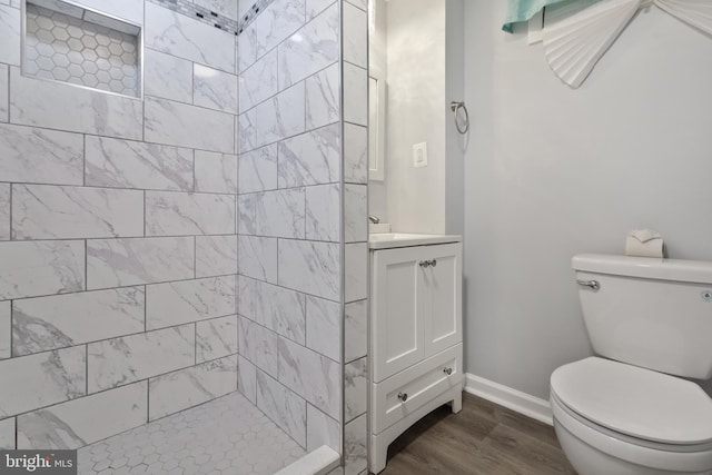 bathroom with wood-type flooring, vanity, a tile shower, and toilet