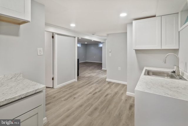 kitchen featuring white cabinets, light stone counters, sink, and light hardwood / wood-style flooring