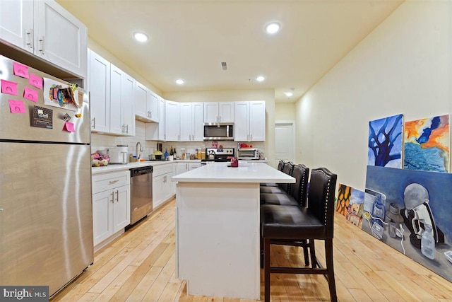 kitchen with white cabinets, appliances with stainless steel finishes, a breakfast bar, light hardwood / wood-style floors, and a center island