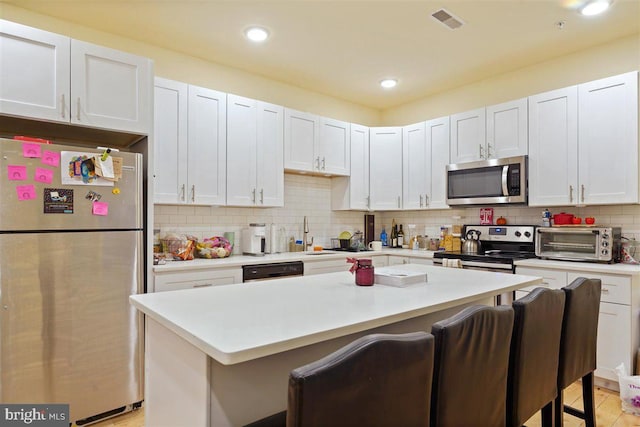 kitchen featuring decorative backsplash, a kitchen island, a kitchen breakfast bar, stainless steel appliances, and white cabinets