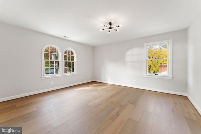 unfurnished room featuring light hardwood / wood-style flooring, a wealth of natural light, and a chandelier