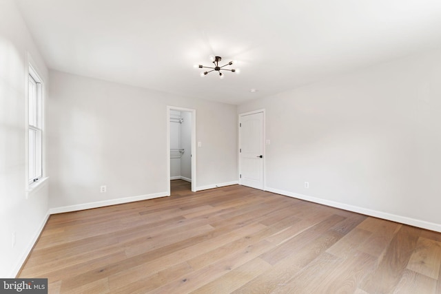 empty room featuring a notable chandelier and light wood-type flooring