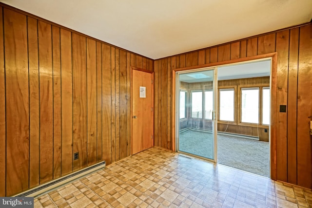 carpeted spare room featuring a baseboard heating unit and wooden walls