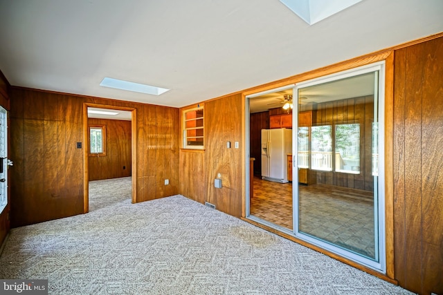 carpeted spare room with wooden walls, a skylight, and ceiling fan