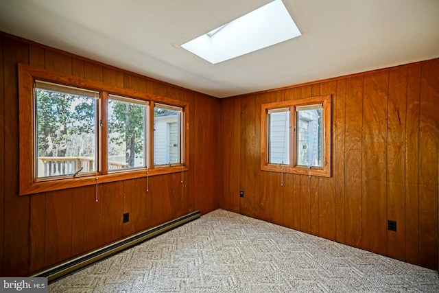 carpeted empty room featuring wood walls, a skylight, and a baseboard heating unit