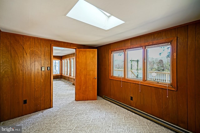 carpeted spare room featuring wood walls, a skylight, a wealth of natural light, and a baseboard heating unit