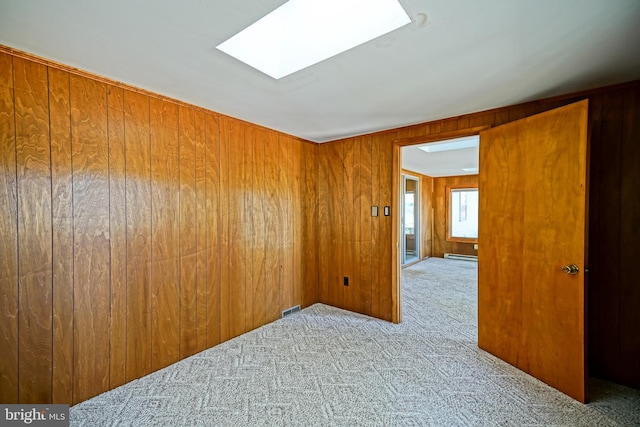 carpeted spare room with baseboard heating, wooden walls, and a skylight