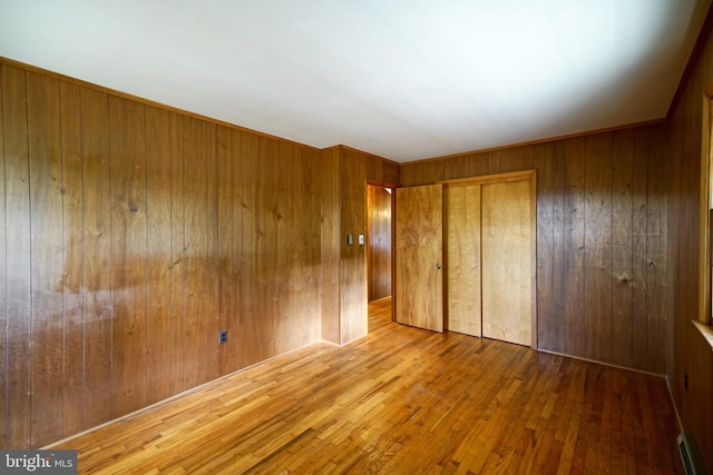 unfurnished bedroom featuring hardwood / wood-style floors, a baseboard heating unit, a closet, and wood walls