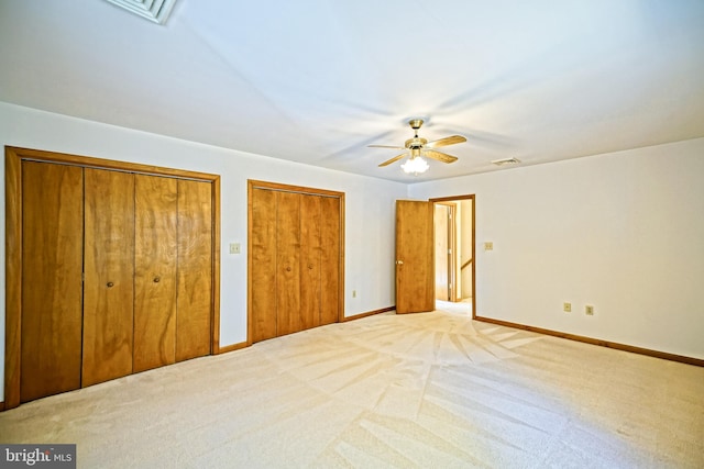 unfurnished bedroom with light carpet, two closets, and ceiling fan