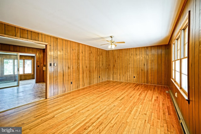 unfurnished room featuring light hardwood / wood-style floors, wooden walls, a baseboard radiator, and ceiling fan