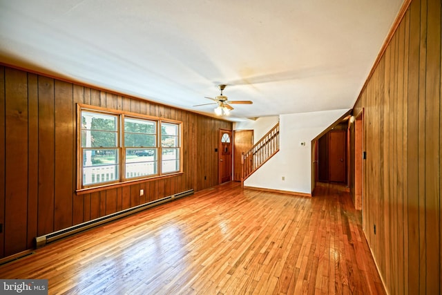 unfurnished living room featuring light hardwood / wood-style floors, a baseboard radiator, wooden walls, and ceiling fan