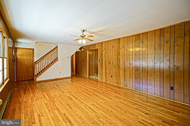 unfurnished living room with wood walls, a baseboard radiator, light wood-type flooring, and ceiling fan