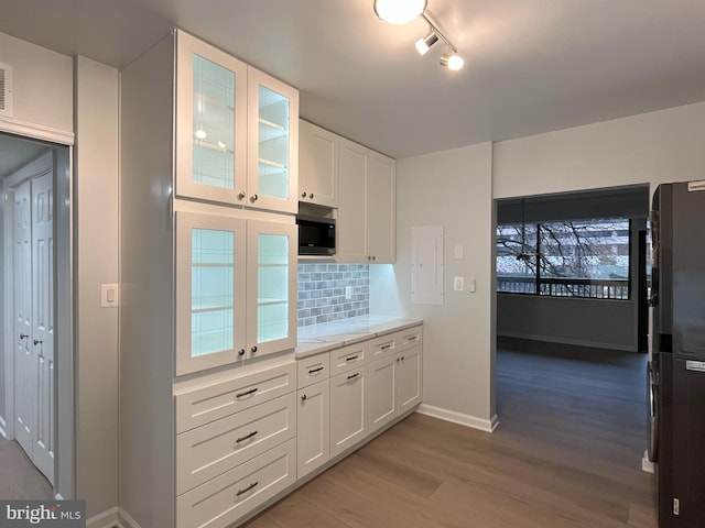 kitchen with decorative backsplash, black refrigerator, hardwood / wood-style flooring, white cabinetry, and stainless steel microwave