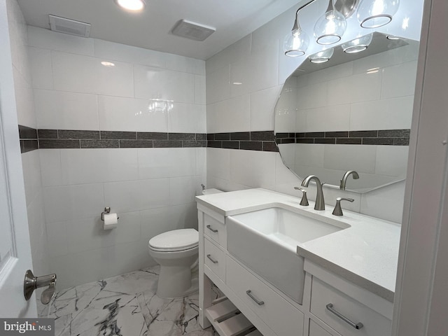 bathroom with vanity, toilet, and tile walls