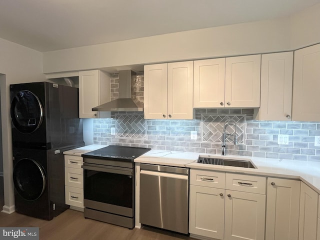 kitchen with sink, light hardwood / wood-style flooring, wall chimney exhaust hood, stacked washer / drying machine, and stainless steel appliances