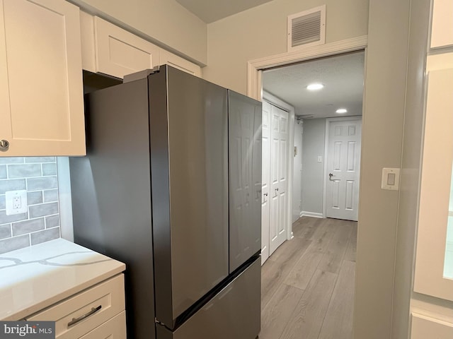 kitchen with stainless steel refrigerator, decorative backsplash, light hardwood / wood-style flooring, and white cabinets