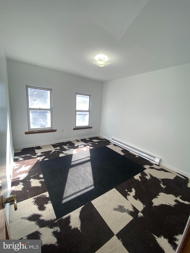 carpeted empty room featuring a baseboard heating unit