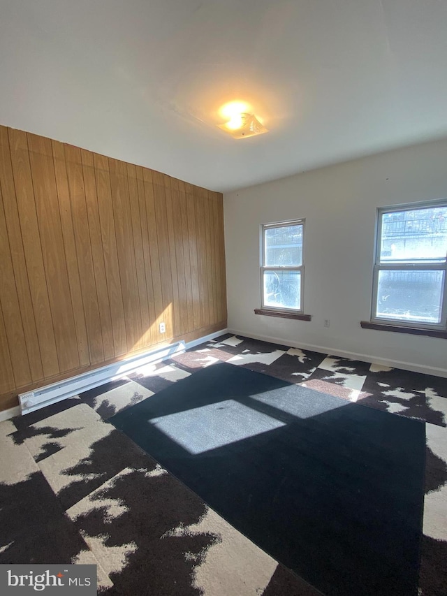 carpeted empty room featuring a baseboard heating unit and wooden walls