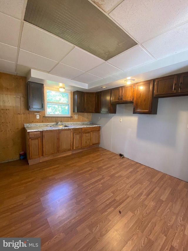 kitchen with a drop ceiling, wood walls, light countertops, wood finished floors, and a sink