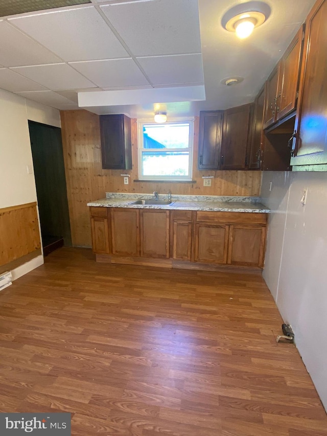 kitchen featuring sink, dark wood-type flooring, a drop ceiling, and wood walls