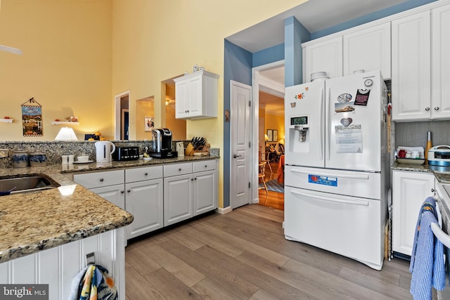 kitchen with white fridge with ice dispenser, light hardwood / wood-style flooring, white cabinets, and dark stone countertops