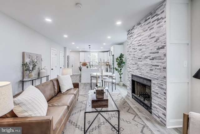 living room featuring sink, light hardwood / wood-style flooring, and a stone fireplace