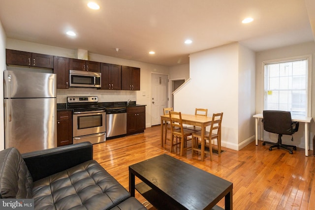 kitchen with dark brown cabinetry, tasteful backsplash, appliances with stainless steel finishes, and light hardwood / wood-style flooring