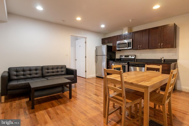 kitchen with tasteful backsplash, stainless steel appliances, dark brown cabinets, and light wood-type flooring