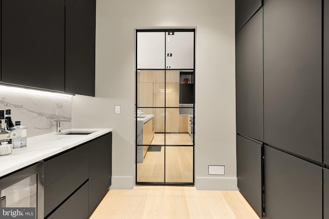 interior space with wine cooler, light hardwood / wood-style floors, light stone countertops, sink, and tasteful backsplash