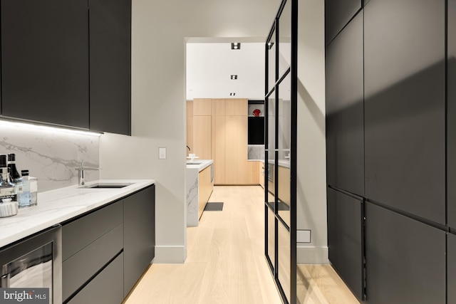 kitchen with wine cooler, light stone countertops, decorative backsplash, sink, and light hardwood / wood-style flooring