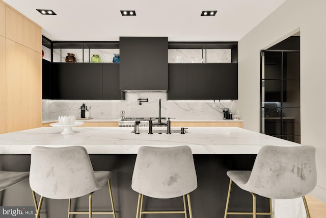 kitchen featuring range hood, a breakfast bar area, light brown cabinetry, and an island with sink