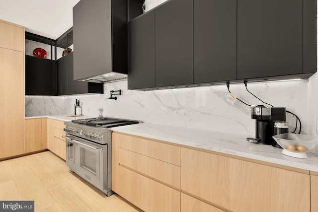 kitchen with light stone countertops, range with two ovens, light brown cabinetry, light hardwood / wood-style floors, and backsplash