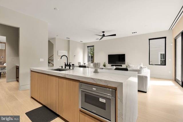 kitchen with a kitchen island with sink, light stone counters, light brown cabinets, sink, and light hardwood / wood-style flooring