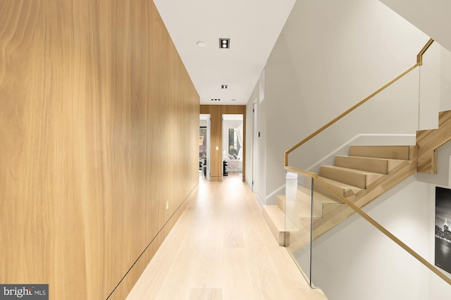 corridor featuring light wood-type flooring and wooden walls