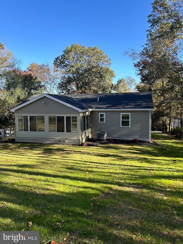 rear view of house with central AC unit and a lawn